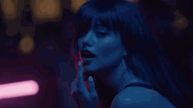 a woman with long black hair is sitting in a dark room with neon lights .