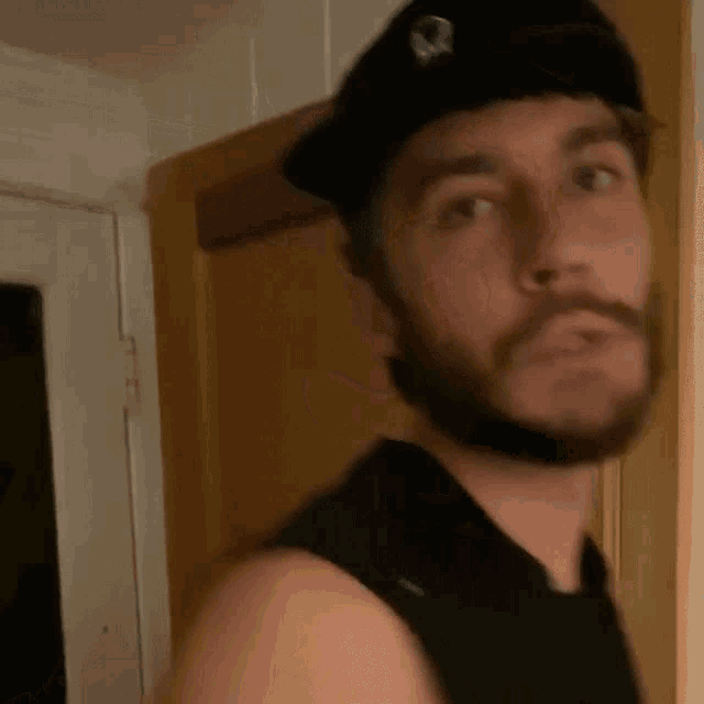 a man with a beard wearing a black hat and a black tank top
