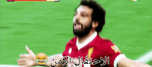 a man with a beard wearing a red shirt is laughing on a soccer field