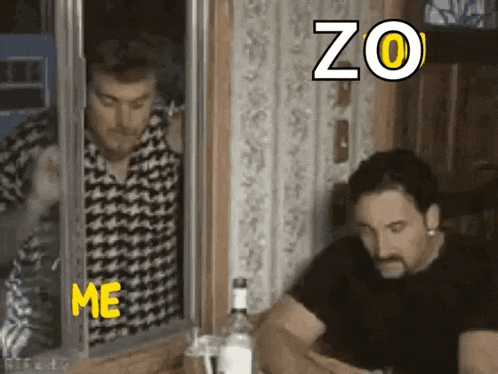 two men are sitting at a table with a bottle of alcohol and looking out of a window .