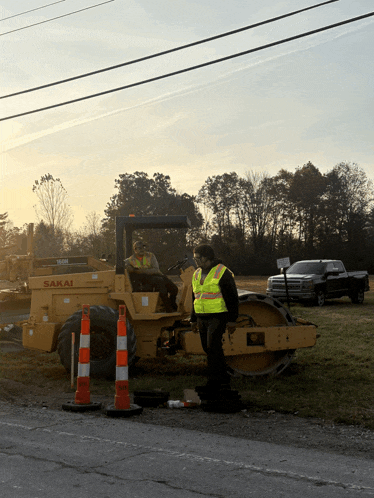 a man in a yellow vest stands in front of a sakai machine
