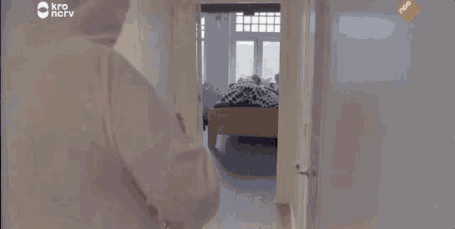 a man is standing in a hallway looking into a bedroom with a bed .