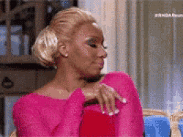 a woman in a pink top is sitting on a couch with her hands on her hips .