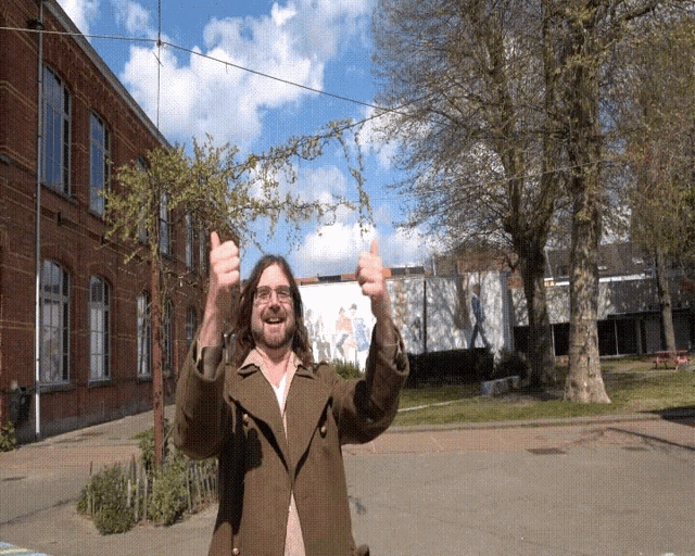 a man giving two thumbs up in front of a building