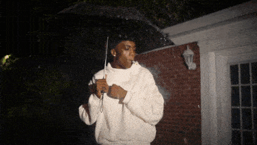 a man in a white sweatshirt holds an umbrella in front of a brick building