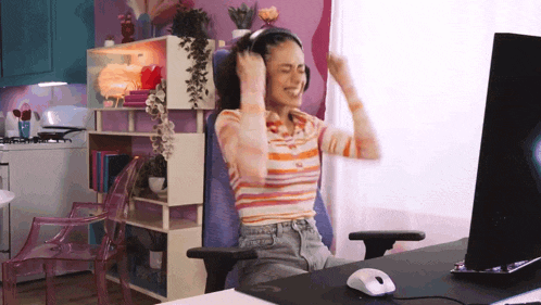 a woman wearing headphones is sitting in front of a computer with her arms in the air