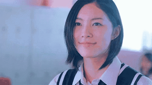 a young woman with short hair is smiling and looking at the camera in a classroom .