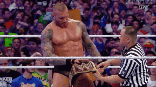 a wrestler is standing in a wrestling ring while a referee holds his belt .