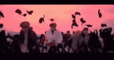 a group of people are dancing in front of a pink sky .