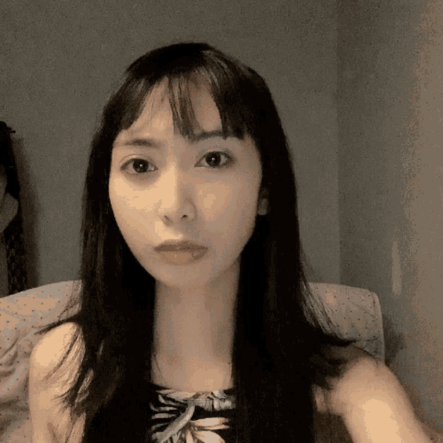 a woman with long black hair and a floral top looks at the camera