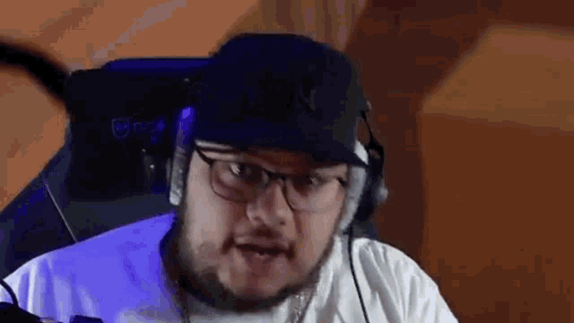 a man wearing glasses and a hat is sitting in a chair with headphones on .