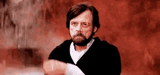 a man with a beard is standing in front of a red wall and making a face .