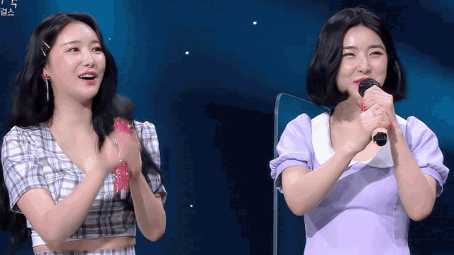 a woman in a purple dress is singing into a microphone next to another woman in a plaid shirt