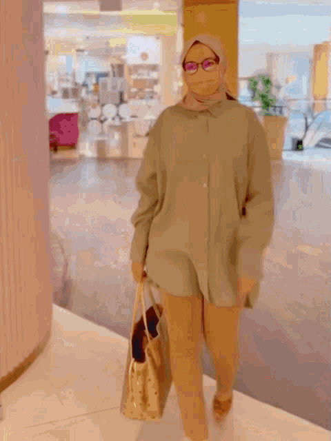 a woman wearing glasses and a hijab is walking in a shopping mall