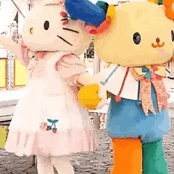 two hello kitty mascots are holding hands and standing next to each other .