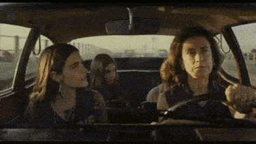 a woman is driving a car with two girls in the back seat
