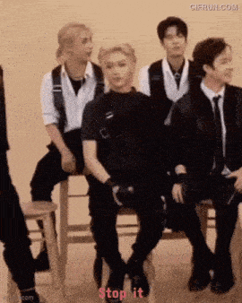 a group of men are sitting on stools and one of them is sitting on a chair .