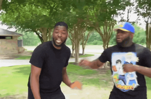 two men are dancing in a park with one wearing a t-shirt that says ' snoop dogg ' on it