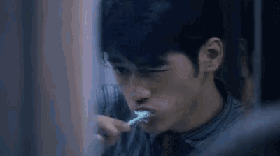 a man is brushing his teeth in front of a mirror in a dark room .
