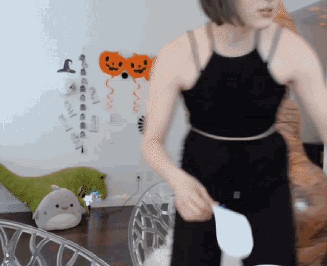 a woman in a black tank top is standing in a room with balloons on the wall