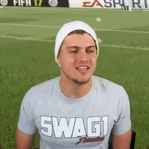 a man wearing a hat and a t-shirt that says swag is sitting on a soccer field .