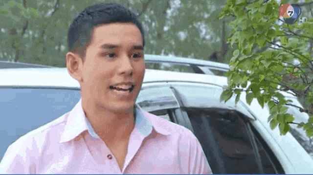 a man in a pink shirt is smiling in front of a white suv .