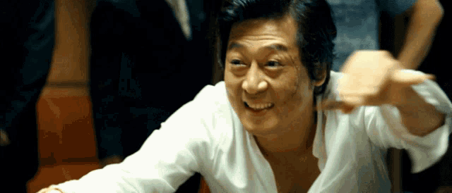 a man in a white shirt is smiling and pointing at something