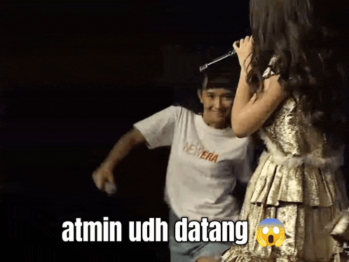 a woman in a gold dress is holding a microphone while a man in a white shirt with the word new era on it