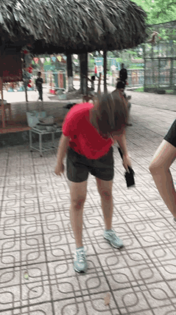 a woman in a red shirt and black shorts stands on a tiled floor