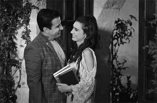 a man and a woman are standing next to each other and the woman is holding a book in her hand .