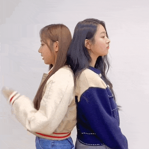 two girls standing back to back wearing sweaters and jeans