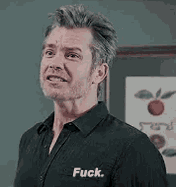 a man in a black shirt is standing in front of a framed picture of an apple and says `` fuck '' .