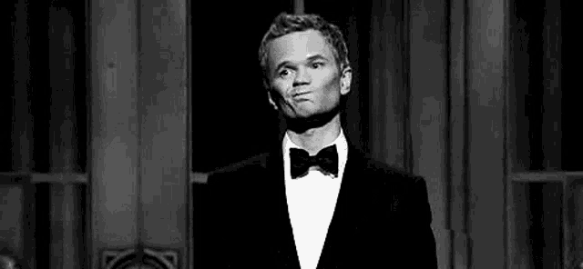 a black and white photo of a man in a tuxedo and bow tie making a funny face .