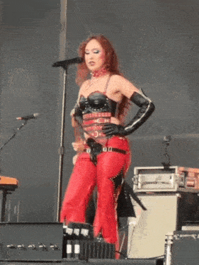 a woman singing into a microphone while wearing red leather pants and black gloves