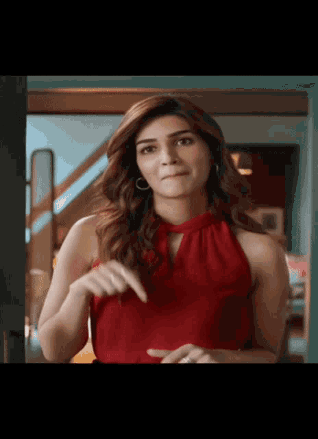 a woman in a red top is making a funny face while pointing at herself .