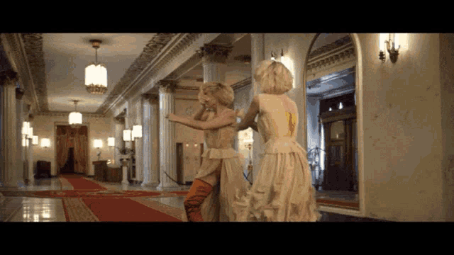 two women are dancing in a hallway with columns