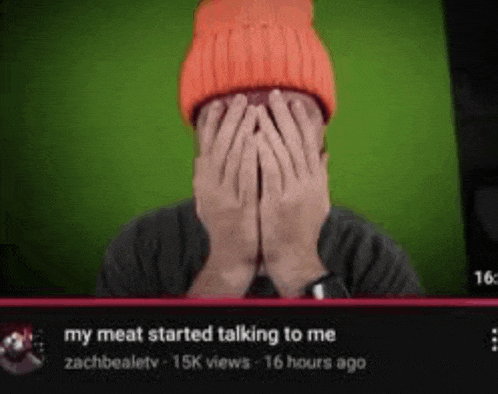 a man wearing an orange beanie is covering his face with his hands while watching a video .
