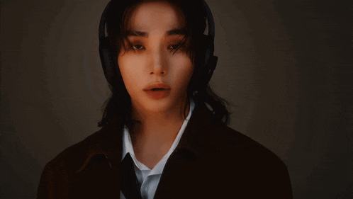a woman wearing headphones and a brown jacket looks at the camera
