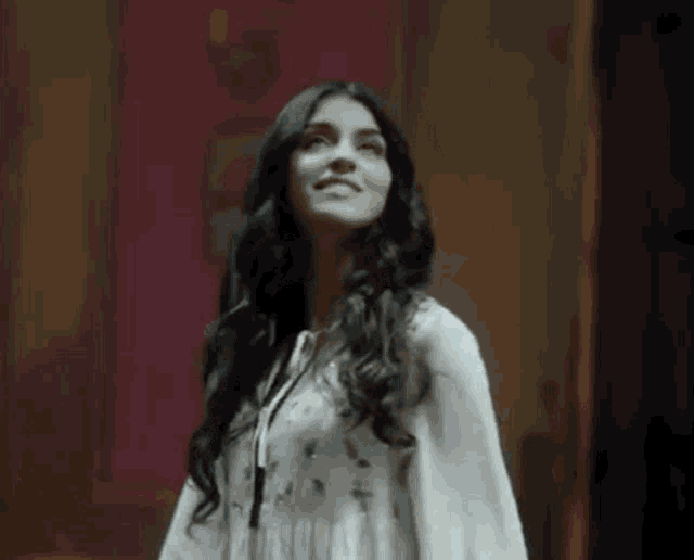 a woman in a white dress is standing in a dark room and smiling .