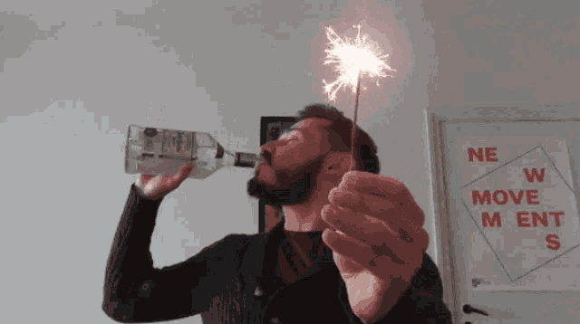 a man drinking from a bottle while holding a sparkler in front of a sign that says new move m ent