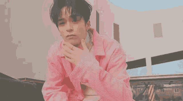 a young man in a pink jacket is sitting on a bench .