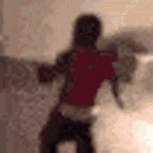 a blurry picture of a person in a red shirt standing in front of a bed .