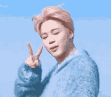 a young man in a blue sweater is making a peace sign