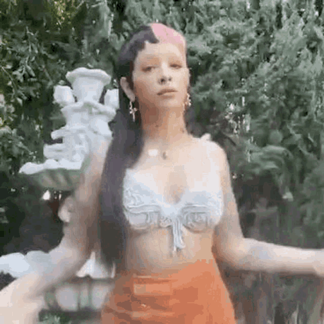 a woman in a crop top and orange skirt is standing in front of a tree .
