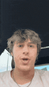 a young man wearing a white t-shirt and a necklace looks surprised