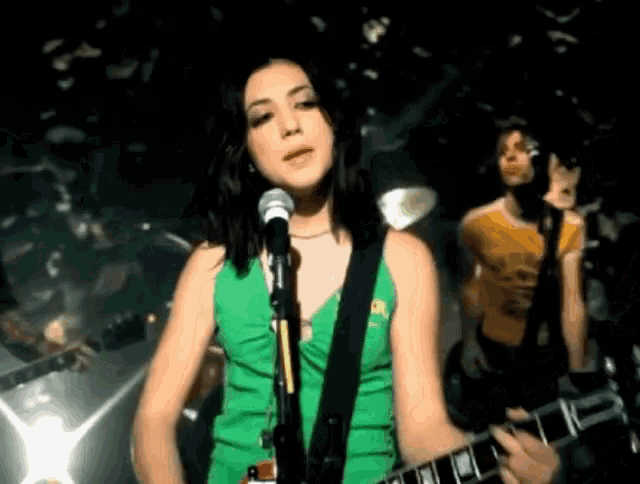 a woman singing into a microphone while a man plays a guitar in a band