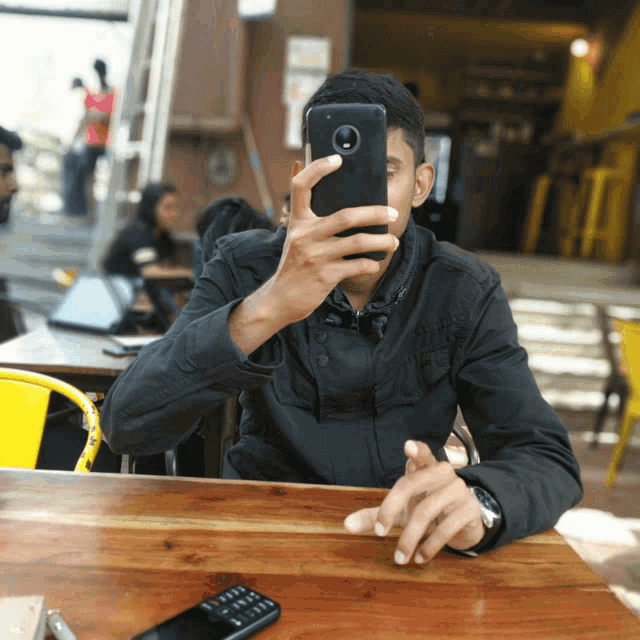 a man sitting at a table taking a selfie with his phone
