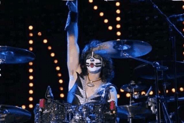a man with a face painted on his face is playing drums on stage .