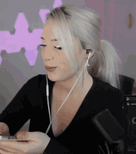 a blonde woman wearing ear buds looks at her phone