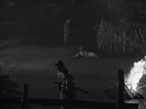 a black and white photo of a man holding a sword standing next to a fire